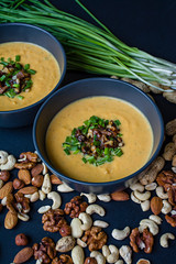 Pumpkin cream soup with herbs and nuts, served in a dark bowl. Proper and healthy food. Vegetarian dish. Dark background.