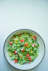 Salad with corn, crab sticks, cucumbers in a white bowl on a white background. Vegetarian salad. Cooking process.
