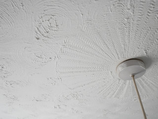 Ceiling rose with paint marks hanging from a swirly patterned ceiling plaster pattern known as Artex was common in the 80s.