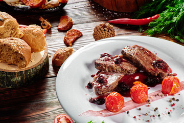 grilled meat medallions and red sauce on a white plate on dark wooden background in beautiful composition among vegetables and spices. Top view. Flat lay