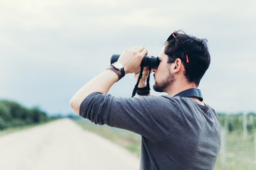 Portrait of young adventure man travelling with binoculars, watching landscape view outdoors. Young brunette man discover nature scenes. Travelling, discovering, vacation concept
