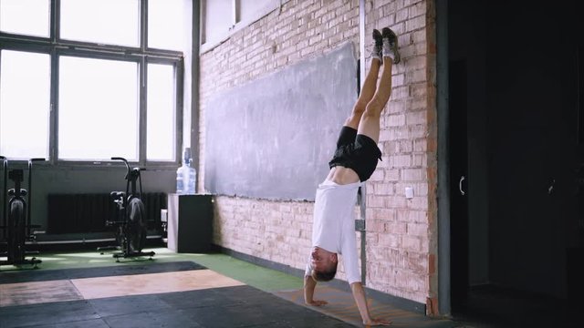 How to do handstand pushup for advanced, hand stand push ups tutorial near the wall. Man wears sport white T-shirt and black shorts. Doing exercizes in gym