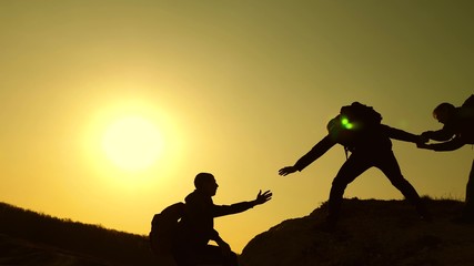 teamwork of business people. travelers climb one after another on rock. joint business. Slow motion. Climbers silhouettes stretch their hands to each other, climbing to top of hill. sport climber.