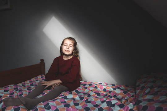 Smiling girl sitting on bed at home with closed eyes