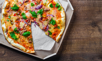 Pizza with Mozzarella cheese, onion,  tuna fish, tomato sauce, pepper, basil. Italian pizza in the in delivery cardboard box on wooden table background