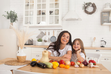 Smiling mom and daughter cook vegetables in the Scandinavian-style kitchen. Healthy food