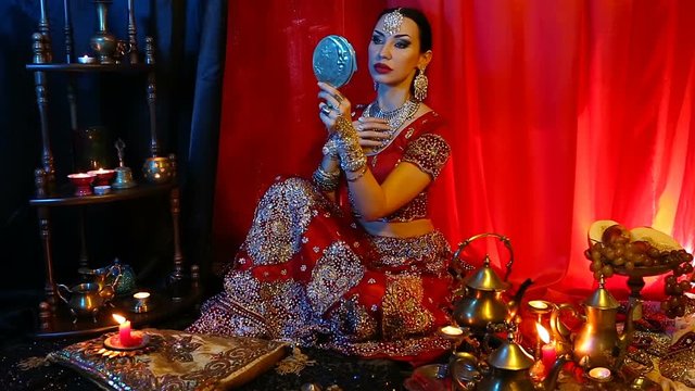 Beautiful young indian woman in traditional Sari clothing with Oriental Jewelry looking in the mirror and trying on jewelry