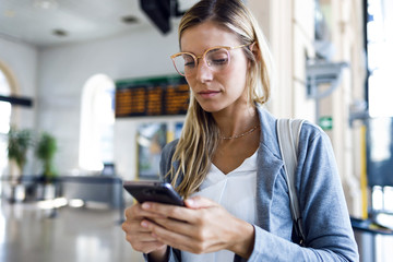 Young woman texting with her mobile phone in the train station hall