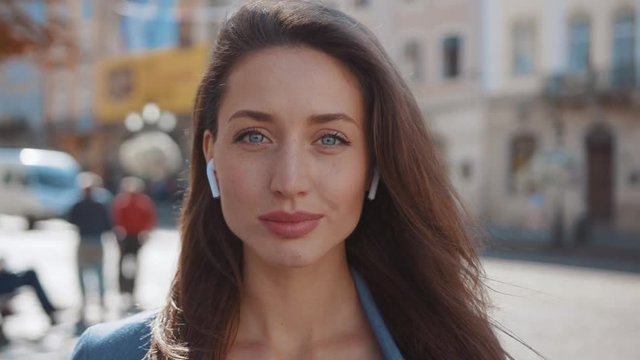 Portrait young face woman with headphones look at camera technology urban city close happiness music outdoors confidence sidewalk relaxed lifestyle close up slow motion