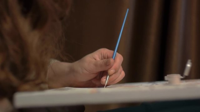 girl's hand with a blue thin tassel paints a picture on canvas