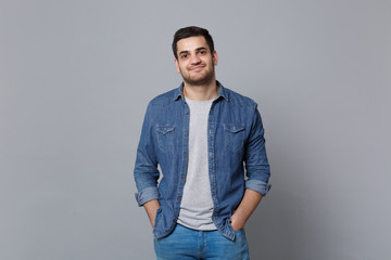 Handsome stylish unshaven young man in denim jeans shirt posing isolated on grey wall background studio portrait. People sincere emotions lifestyle concept. Mock up copy space. Looking camera smile.