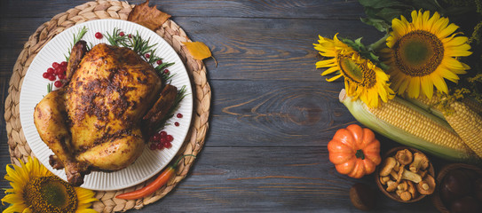 Roasted whole chicken or turkey with autumn vegetables for thanksgiving dinner on wooden background. Thanksgiving Day concept. Top view, long web format