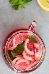 A refreshing drink of hibiscus, mint and lemon in a glass jug on a gray background.