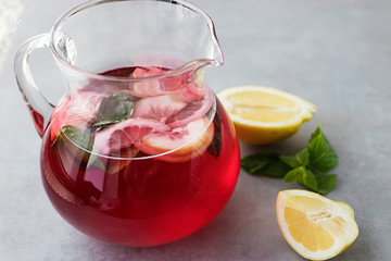 A refreshing drink of hibiscus, mint and lemon in a glass jug on a gray background.