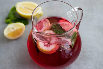 A refreshing drink of hibiscus, mint and lemon in a glass jug on a gray background.