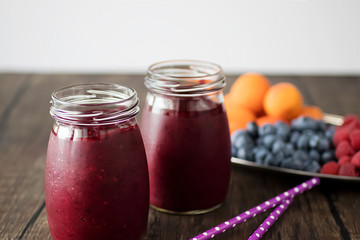 Fruit and berry smoothies and fresh apricots, raspberries and blueberries on an oval metal plate. Gray background.