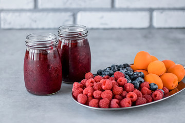 Fruit and berry smoothies and fresh apricots, raspberries and blueberries on an oval metal plate. Gray background.