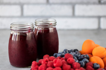 Fruit and berry smoothies and fresh apricots, raspberries and blueberries on an oval metal plate. Gray background.
