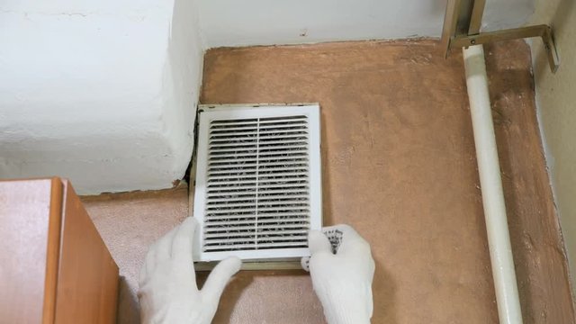  man in gloves opens a dusty ventilation grill to clean the ventilation 