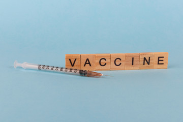  Syringe and the word vaccine from wooden letters on a light blue background. Concept of primary prevention, control diseases,themes of supporters and opponents of vaccination, health problems,the dan