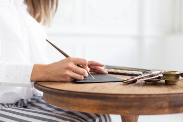 Woman calligrapher is holding a pen with ink and signs a card in handwritten font. Close-up. Soft...