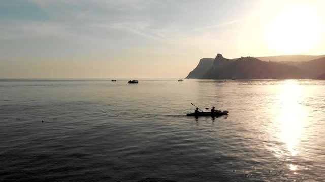 Aerial view of a kayak in the middle of the sea. Drone flight above two people kayakers paddling at sunset. Colorful sport kayak silhouette. Beautiful sea landscape at summer sunset.