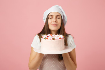 Housewife female chef cook confectioner or baker in apron white t-shirt, toque chefs hat hold in hand cake on stand plate isolated on pink pastel background in studio. Mock up copy space food concept.
