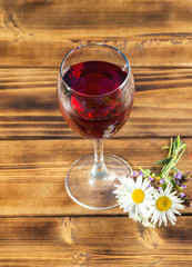Glass of red wine with meadow flowers on rusty wooden table