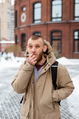 A bearded young man smokes a cigarette in winter