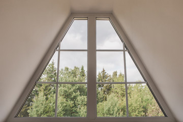 View of the green trees and the forest from the window in the attic - an unusual shape window - comfort and fresh air