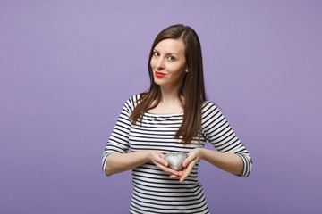 Young brunette woman girl in casual striped clothes posing isolated on violet purple background studio portrait. People sincere emotions lifestyle concept. Mock up copy space. Hold silver argent heart