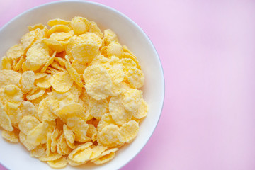 Cornflakes dry breakfast in a white bowl on a pink backgroud. space for text