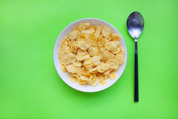 Cornflakes dry breakfast in a white bowl with a spoon on a green backgroud. top view