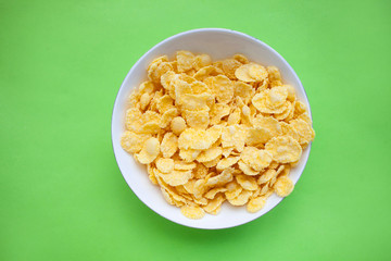 Cornflakes dry breakfast in a white bowl on a green backgroud. top view