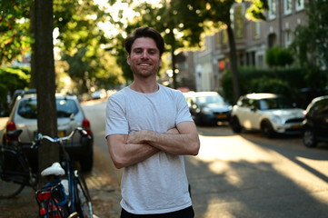 Male master student smiling and standing with his arms crossed in a traditional street in Amsterdam, the Netherlands
