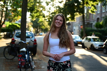 Fototapeta na wymiar A spontaneous and happy young woman standing in a beautiful Dutch street by sunset