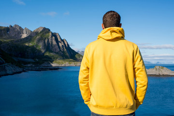 A young man in a yellow hoodie outdoor enjoy the northern beauty. Ocean and rocks landscape. Scenic view. Travel, adventure. Sense of freedom, lifestyle. Lofoten Islands, Norway. Summer in Scandinavia