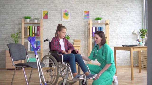 doctor examines the leg of a teenage girl with a disability in a wheelchair