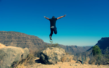Man jumping whit arms raised in the mountain on a sunny day, feeling of freedom, lifestyle concept.