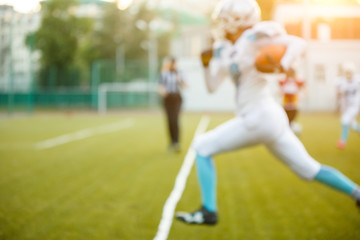 Photo of young athlete playing American football running on green field on summer