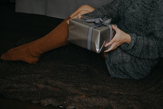 Soft cozy photo of woman in warm sweater on the bed with a gift in their hands. Girl sitting on plaid