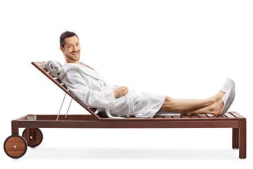 Cheerful young man in a bathrobe relaxing on a lounge chair and smiling at the camera