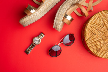 Flat lay, Wicker fashion bag, sunglasses, tropical bananas and expensive watches and women's shoes. Summer fashion, the concept of the holiday. On a bright red background.