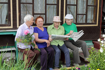Four Russian women sit on a bench at the village house and actively discuss the news from the newspaper. Country life.