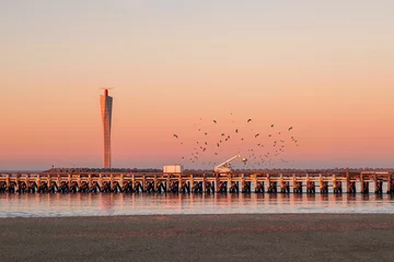 Foto auf Leinwand Sunset  on the old wooden pier of Ostend, with modern radar tower in the background. Lots of seagulls flying around. © Erik_AJV