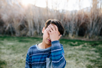 Boy outside appears sad as he covers part of his face with his hand