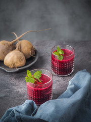 Two glasses of beetroot smoothie with mint leaves on dark table.