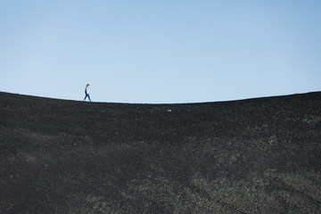 woman walks alone on a black basalt sand concave horizon line