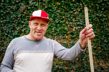 Portrait of a senior man in a ball cap with toothy grin doing yardwork