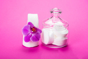 Obraz na płótnie Canvas Cotton sponges in a glass jar on a pink background with an orchid flower